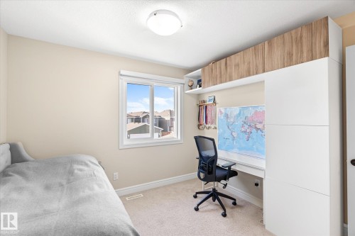 Integrated built-in desk with overhead wood-finish cabinetry, white shelving, and a white window frame - 6864 Evans Wynd, Edmonton, AB - Indoor Photo Showing Bedroom