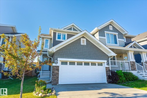 Contemporary home with a two-car garage, stone accents, and a covered porch with white railing - 6864 Evans Wynd, Edmonton, AB - Outdoor With Facade
