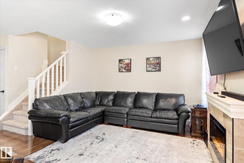 Living area featuring wood-finish flooring, a carpeted staircase with white railings, and a tiled fireplace surround - 6864 Evans Wynd, Edmonton, AB - Indoor Photo Showing Living Room