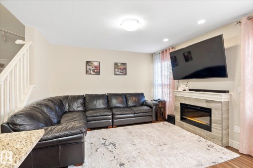 Living area featuring a tiled fireplace with mantel, recessed lighting, ceiling-mounted light fixture, and wood-finish flooring - 6864 Evans Wynd, Edmonton, AB - Indoor Photo Showing Living Room With Fireplace