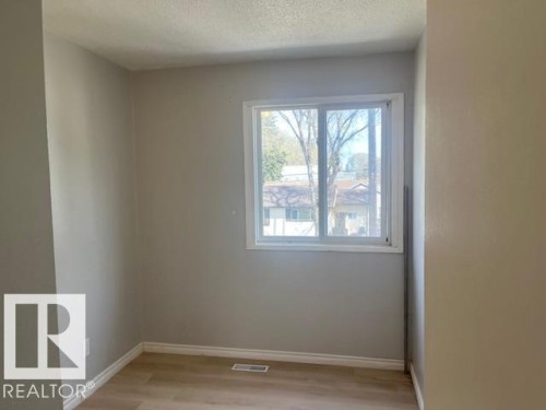 Bright room featuring a large window, light-toned walls, wood-finish flooring, white baseboards, and a white window frame - 6117 120 Avenue, Edmonton, AB - Indoor Photo Showing Other Room