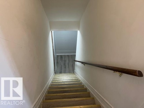 Stairwell featuring a dark wood handrail, white painted walls, and wood-finish stair treads with brass-toned strips - 6117 120 Avenue, Edmonton, AB - Indoor Photo Showing Other Room