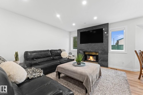 Living area featuring a floor-to-ceiling dark stone fireplace surround, inset fireplace, recessed lighting, and wood-finish flooring - 362 Blackburn Drive E, Edmonton, AB - Indoor Photo Showing Living Room With Fireplace