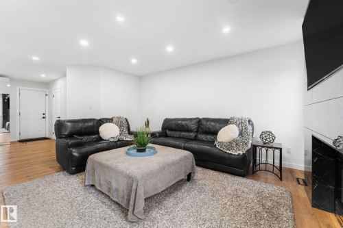 Bright living space featuring recessed lighting, light wood-finish flooring, a white paneled entry door, and a fireplace with black marble surround and white tiled facade - 362 Blackburn Drive E, Edmonton, AB - Indoor