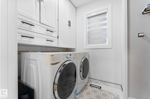 Laundry area featuring white shaker-style cabinetry with matte black hardware, a window with horizontal blinds, and a patterned area rug over tile flooring - 362 Blackburn Drive E, Edmonton, AB - Indoor Photo Showing Laundry Room