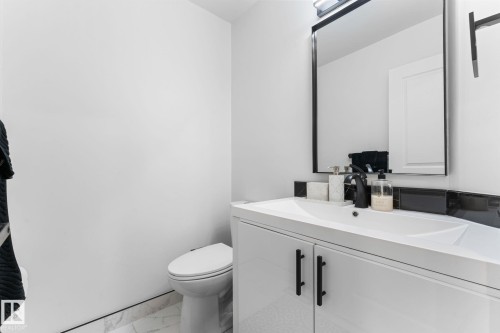 Modern bathroom featuring a white vanity with integrated sink, matte black faucet, framed mirror with integrated lighting, a white toilet, and marble-look tile flooring - 362 Blackburn Drive E, Edmonton, AB - Indoor Photo Showing Bathroom