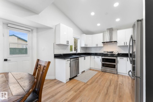 Modern kitchen featuring white cabinetry, dark countertops, a hexagonal tile backsplash, stainless steel appliances, and wood-finish flooring - 362 Blackburn Drive E, Edmonton, AB - Indoor Photo Showing Kitchen With Upgraded Kitchen