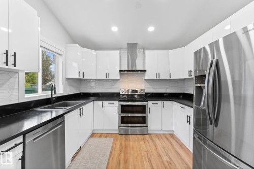 Modern kitchen featuring white cabinetry with matte black hardware, dark countertops, a tile backsplash, wood-finish flooring, and stainless steel appliances - 362 Blackburn Drive E, Edmonton, AB - Indoor Photo Showing Kitchen With Double Sink With Upgraded Kitchen