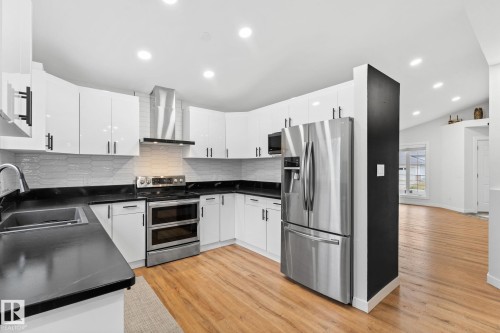 Modern kitchen featuring white cabinetry with black hardware, black countertops, stainless steel appliances, and a subway tile backsplash - 362 Blackburn Drive E, Edmonton, AB - Indoor Photo Showing Kitchen With Double Sink With Upgraded Kitchen