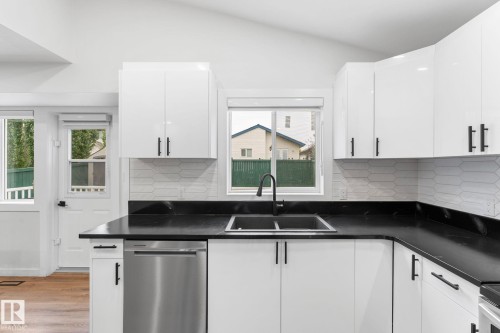 Modern kitchen featuring white cabinetry, black countertops, a stainless steel dishwasher, and a dual basin sink with a black faucet - 362 Blackburn Drive E, Edmonton, AB - Indoor Photo Showing Kitchen With Double Sink