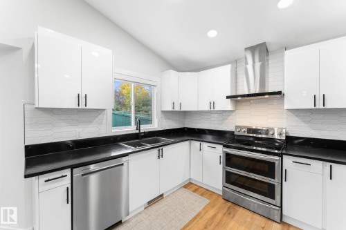 Modern kitchen featuring white cabinetry with black hardware, dark countertops, a stainless steel double oven range, and a coordinating dishwasher - 362 Blackburn Drive E, Edmonton, AB - Indoor Photo Showing Kitchen With Double Sink