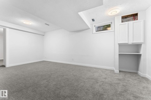 Spacious room featuring neutral carpeting, white walls, and a built-in cabinet with open shelving - 362 Blackburn Drive E, Edmonton, AB - Indoor Photo Showing Other Room