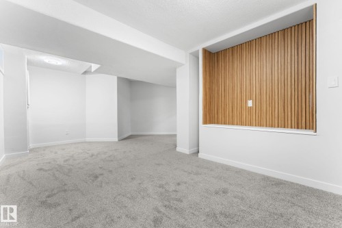 Spacious room featuring light grey carpeting, white walls, and a distinctive built-in alcove with vertical wood paneling - 362 Blackburn Drive E, Edmonton, AB - Indoor Photo Showing Other Room