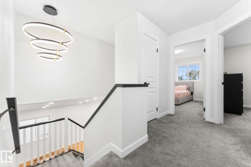 Contemporary hallway featuring a multi-tiered circular pendant light, black handrails, white balusters, and gray carpeted flooring - 362 Blackburn Drive E, Edmonton, AB - Indoor Photo Showing Other Room