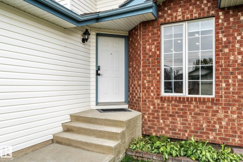 Exterior showcasing a brick facade, white siding, a white entry door with a smart lock, concrete steps, and a double-pane window with grid inserts - 362 Blackburn Drive E, Edmonton, AB - Outdoor With Exterior