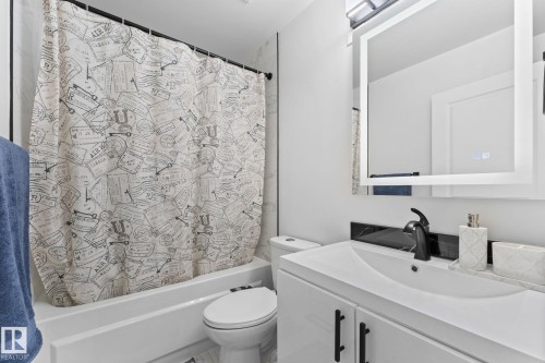 Bathroom featuring a built-in bathtub with white surround, a white vanity with integrated sink, black countertop backsplash, and a wall-mounted mirror with integrated lighting - 362 Blackburn Drive E, Edmonton, AB - Indoor Photo Showing Bathroom