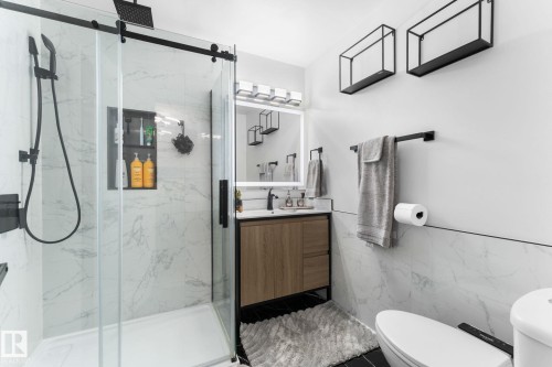 Contemporary bathroom featuring a glass-enclosed shower with matte black fixtures, a built-in shower niche, and white marble-look wall tiling - 362 Blackburn Drive E, Edmonton, AB - Indoor Photo Showing Bathroom
