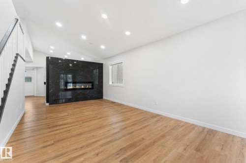 Spacious living area featuring light wood-finish flooring, a contemporary fireplace with a dark marble-patterned surround, recessed lighting, and a window with white louvered blinds - 362 Blackburn Drive E, Edmonton, AB - Indoor With Fireplace