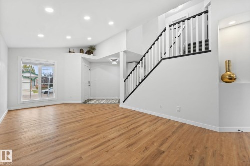 Spacious entry and living area featuring wood-finish flooring, a contemporary staircase with black and white railings, recessed ceiling lighting, and a built-in wall niche - 362 Blackburn Drive E, Edmonton, AB - Indoor Photo Showing Other Room