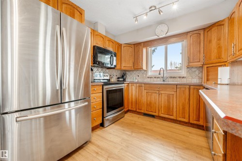 Kitchen featuring wood cabinetry, stainless steel appliances, a window above the sink, and a tiled backsplash - 2437 89 Street, Edmonton, AB - Indoor Photo Showing Kitchen With Double Sink