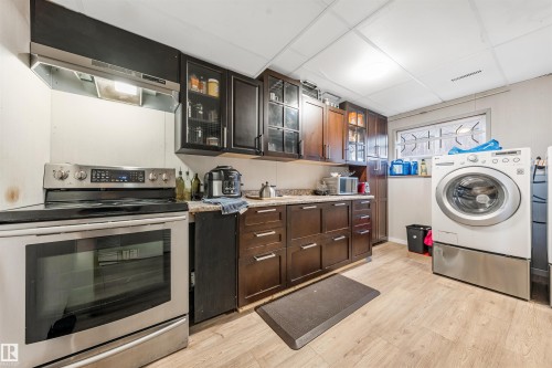 This well-equipped kitchen features dark wood cabinetry, a stainless steel range with an overhead exhaust hood, and light-colored flooring - 2437 89 Street, Edmonton, AB - Indoor Photo Showing Laundry Room