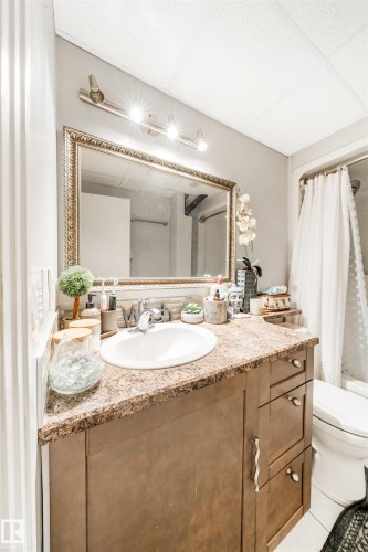 The bathroom features a vanity with a countertop and an integrated sink, a framed mirror, and a shower with a curtain - 2437 89 Street, Edmonton, AB - Indoor Photo Showing Bathroom