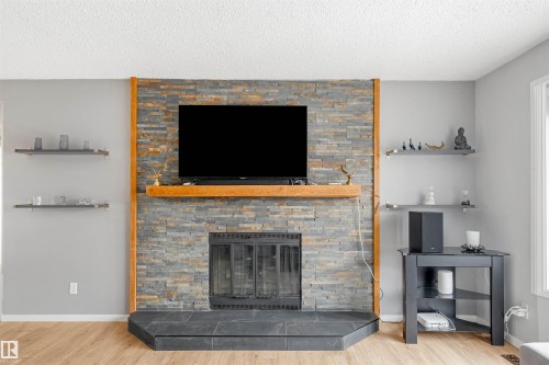 Living area featuring a floor-to-ceiling stone fireplace with a wood mantel, a black hearth, and wood flooring - 2437 89 Street, Edmonton, AB - Indoor Photo Showing Living Room With Fireplace