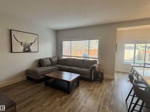 Living area featuring wood-finish flooring, light-toned wall paint, and a large window with horizontal blinds - 11 James Crescent, St. Albert, AB - Indoor Photo Showing Living Room