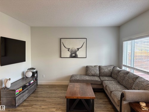 Living area featuring wood-finish flooring, ample natural light from a large window with blinds, and white baseboards - 11 James Crescent, St. Albert, AB - Indoor Photo Showing Living Room