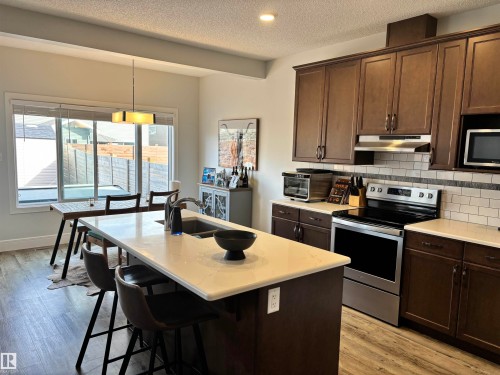 Modern kitchen featuring dark wood cabinetry, light countertops, stainless steel appliances, and wood-finish flooring - 11 James Crescent, St. Albert, AB - Indoor Photo Showing Kitchen