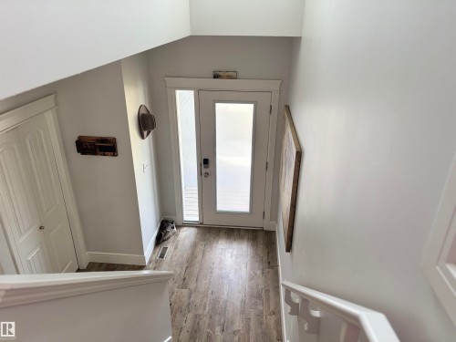 Entryway featuring a white paneled door with frosted glass sidelight, wood-finish flooring, white baseboards, and a built-in closet with white bifold doors - 11 James Crescent, St. Albert, AB - Indoor Photo Showing Other Room