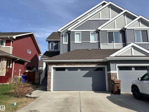 Contemporary multi-level exterior featuring grey horizontal and vertical siding, white trim accents, a shingled roof, stacked stone detailing, and an integrated garage with a grey door - 11 James Crescent, St. Albert, AB - Outdoor With Facade