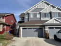 Contemporary multi-level exterior featuring grey horizontal and vertical siding, white trim accents, a shingled roof, stacked stone detailing, and an integrated garage with a grey door - 11 James Crescent, St. Albert, AB  - Outdoor With Facade 