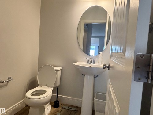 Powder room featuring a pedestal sink with a chrome faucet, oval mirror, and wood-finish flooring - 11 James Crescent, St. Albert, AB - Indoor Photo Showing Bathroom