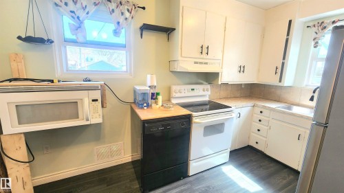 Kitchen featuring wood-finish flooring, white cabinetry with dark hardware, a corner sink, a white electric range, and a black dishwasher - 12139 81 Street, Edmonton, AB - Indoor Photo Showing Kitchen