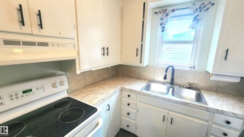 Kitchen featuring white cabinetry with matte black hardware, a dual basin stainless steel sink with a matte black faucet, and a tiled backsplash - 12139 81 Street, Edmonton, AB - Indoor Photo Showing Kitchen With Double Sink