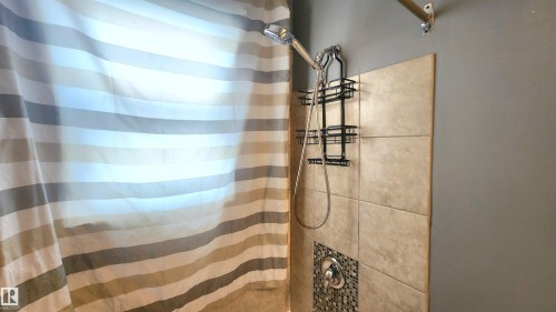 Tiled shower surround featuring a mosaic accent band, a multi-function shower head, and a wall-mounted storage caddy - 12139 81 Street, Edmonton, AB - Indoor Photo Showing Bathroom