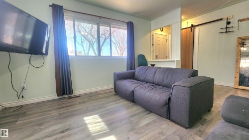 Spacious living area featuring wood-finish flooring, a large window with natural light, and a modern barn door - 12139 81 Street, Edmonton, AB - Indoor