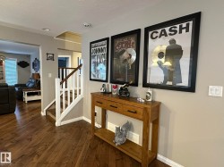 Rich wood-finish flooring provides a warm foundation, complemented by a staircase featuring white risers and a dark wood handrail - 