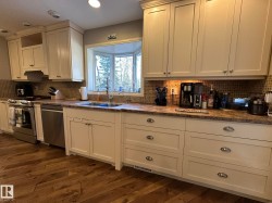 Kitchen featuring white cabinetry, stone-look countertops, a tiled backsplash, and wood-finish flooring - 