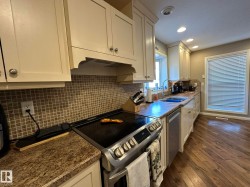 Kitchen featuring light-toned cabinetry, a mosaic tile backsplash, granite-finish countertops, and wood-finish flooring - 