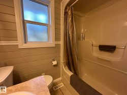 Bathroom featuring shiplap wall paneling, a full bathtub with shower, a frosted window, and tile flooring - 