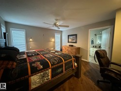 Bedroom featuring rich wood-finish flooring, a ceiling fan with integrated lighting, and dual windows with blinds - 