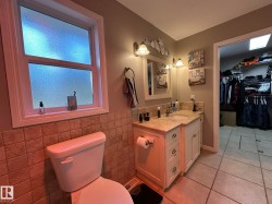Bathroom featuring a window with privacy glass, a vanity with a light-colored countertop and integrated sink, a built-in mirror with sconce lighting, and a neutral tile wainscoting - 