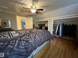 Vaulted ceiling with a ceiling fan light fixture, wood-finish flooring, built-in shelving, two open closets, and a paneled wall finish - 