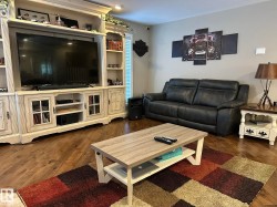 Living area featuring wood-finish flooring, a built-in media center with open shelving and glass-front cabinets, and neutral wall paint - 