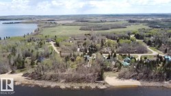 Aerial perspective showcasing a community of properties nestled among abundant trees, fronting a body of water with sandy shores - 