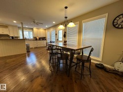 Open-concept kitchen and dining area featuring wood-finish flooring, white cabinetry, a kitchen island with a breakfast bar, and multiple windows with blinds - 