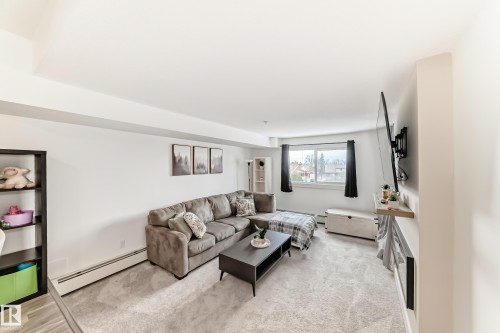 The living area features a carpeted floor, a large window, and light-colored walls - 307 9504 182 Street Nw, Edmonton, AB - Indoor Photo Showing Living Room