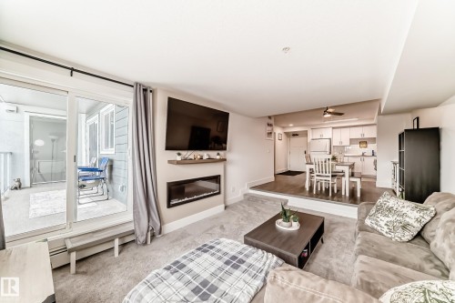 Living area featuring carpeted floors, a wall-mounted electric fireplace, and a sliding glass door leading to an outdoor balcony - 307 9504 182 Street Nw, Edmonton, AB - Indoor Photo Showing Living Room With Fireplace